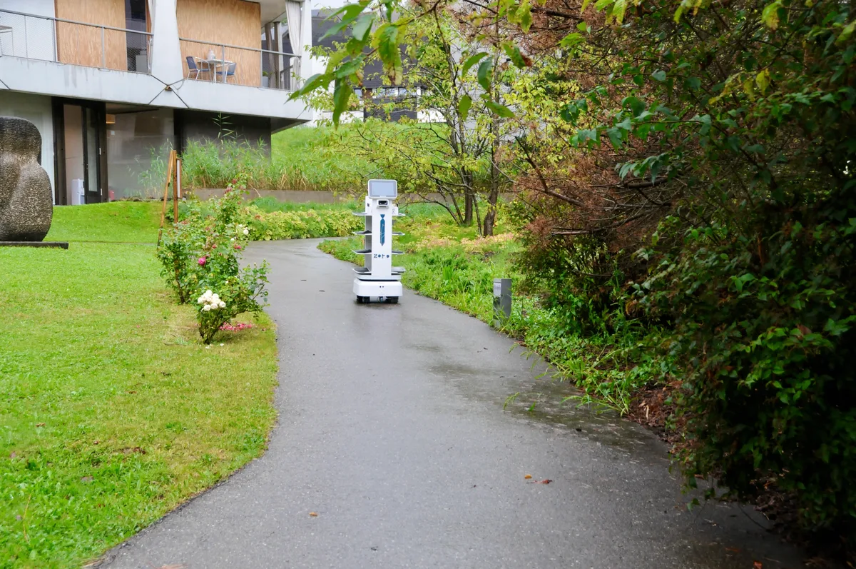 Man sieht einen Serviceroboter durch den Park der Zollinger Stiftung fahren.